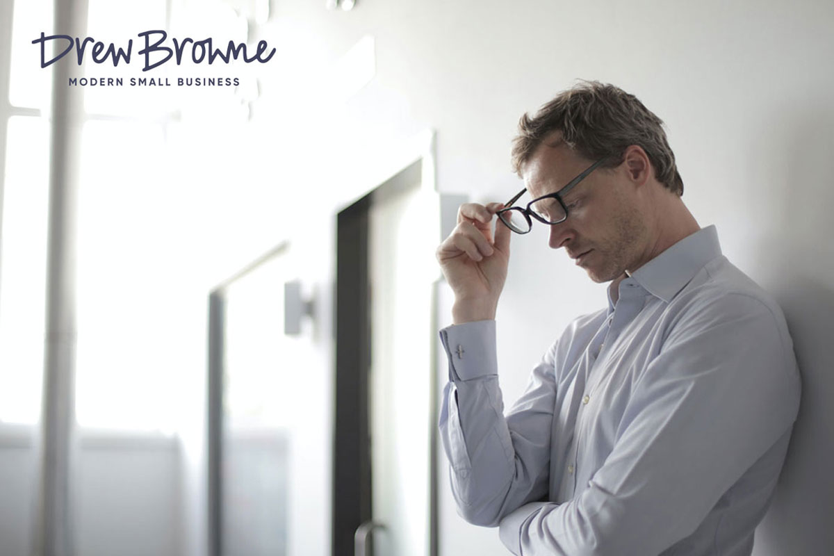 A man in a business shirt taking off his glasses as he stands in a corridor thinking about an idea