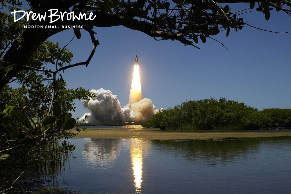 A photo at dusk of the long range launch of a rocket in the distance framed boy overhead trees wall reflected in water below