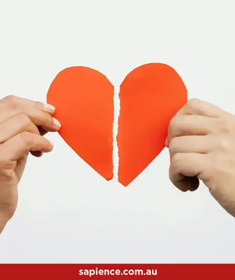a red paper shaped heart being torn in two by separate hands